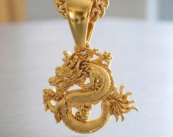 May include: A gold-colored pendant necklace featuring a detailed dragon design. The dragon is intricately sculpted with scales, claws, and a flowing mane. The pendant hangs from a thick, gold chain, creating a bold and eye-catching accessory.