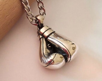 May include: A silver boxing glove pendant necklace. The pendant is detailed and realistic, with a textured surface. The necklace is made of a silver chain.