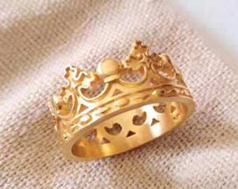 May include: A gold-colored crown ring with intricate details. The ring is made of metal and has a smooth, polished finish.