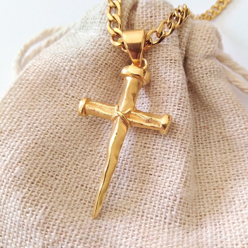 May include: Gold-toned necklace with a large, detailed cross pendant. The cross is shaped like a nail with a pointed end.
