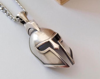 May include: Silver pendant necklace featuring a detailed Spartan helmet design. The helmet is silver with black accents and has a textured finish.
