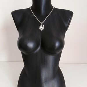 May include: A silver necklace with a pendant in the shape of the Ukrainian coat of arms, displayed on a black mannequin. The pendant is a stylized trident design. The necklace chain is a fine, linked style.