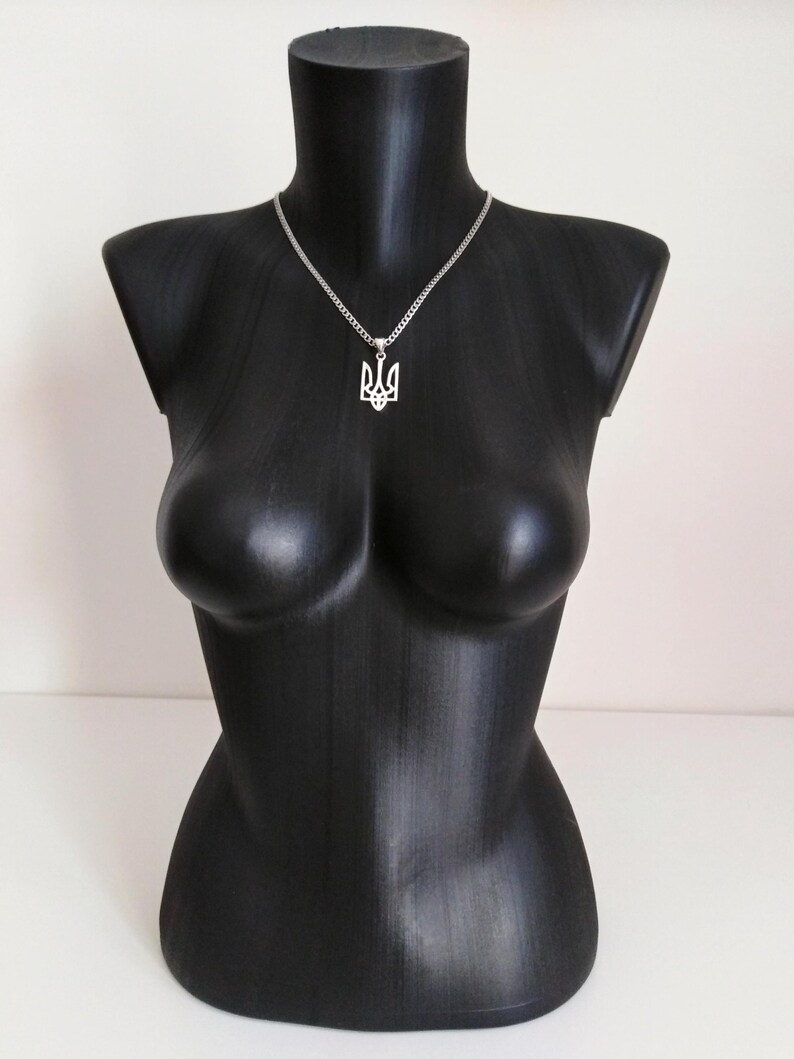 May include: A silver necklace with a pendant in the shape of the Ukrainian coat of arms, displayed on a black mannequin. The pendant is a stylized trident design. The necklace chain is a fine, linked style.