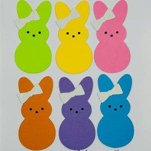 May include: Six colorful bunny cutouts in green, yellow, pink, orange, purple, and blue. Each bunny has a white glitter bow and black dot eyes. The text "Jobzcreations" is at the bottom.