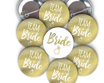 May include: Eight gold and white round buttons with the text "Team Bride" and one white button with the text "Bride".