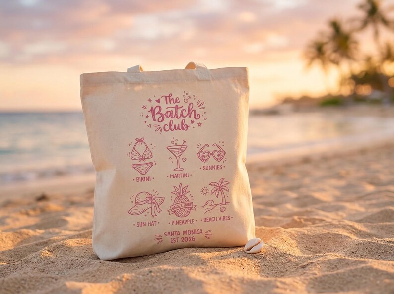May include: A cream canvas tote bag with a pink design. It features beach-themed illustrations and the text "The Batch Club." The bag includes images of a bikini, martini, sunglasses, sun hat, pineapple, and palm trees. The text "Santa Monica EST 2026" is also included.