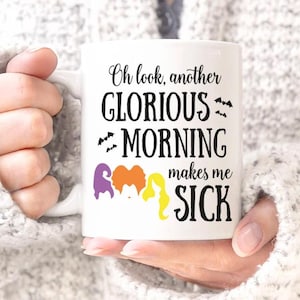 Peut inclure: Une tasse en céramique blanche avec un motif noir qui dit "Oh look, another glorious morning makes me sick". Le motif comprend également trois sorcières avec des cheveux violets, orange et jaunes.