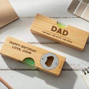 May include: Two wooden level tools with engraved text. One reads "DAD THE MAN, THE MYTH, THE LEVEL" and the other says "HAPPY BIRTHDAY LOVE, JOHN". One has a bottle opener. Both have a green bubble level.
