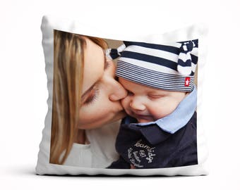 May include: A white pillow featuring a photograph of a woman kissing a baby on the cheek. The baby is wearing a blue and white striped hat with a red star.