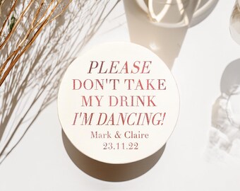 Könnte beinhalten: Ein runder, cremefarbener Untersetzer mit dem Text "PLEASE DON'T TAKE MY DRINK I'M DANCING!" in einem rötlich-braunen Farbton. Der Untersetzer enthält auch die Namen "Mark & Claire" und das Datum "23.11.22".