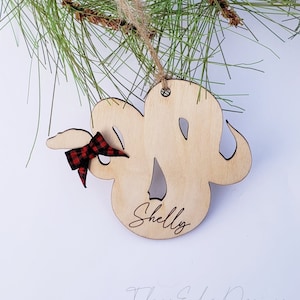 May include: A wooden snake ornament with a red and black plaid bow. The ornament is personalized with the name "Shelly" and the words "Talons Edge Designs".