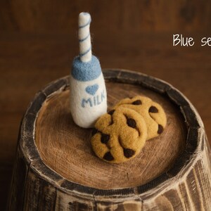 Puede incluir: Una botella de leche de fieltro con tapa azul y pajita a rayas azules y blancas, junto a tres galletas de fieltro con pepitas de chocolate. La botella de leche tiene un coraz&oacute;n azul y la palabra "MILK". El texto "Blue set" est&aacute; en la esquina superior derecha.