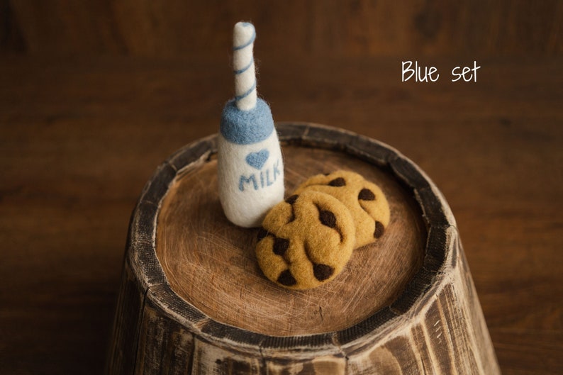 Puede incluir: Una botella de leche de fieltro con tapa azul y pajita a rayas azules y blancas, junto a tres galletas de fieltro con pepitas de chocolate. La botella de leche tiene un coraz&oacute;n azul y la palabra "MILK". El texto "Blue set" est&aacute; en la esquina superior derecha.
