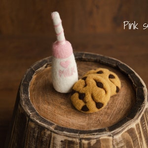 Puede incluir: Una botella de leche rosa y blanca afieltrada con una parte superior rosa y un coraz&oacute;n que dice "MILK" junto a dos galletas con chispas de chocolate. Los art&iacute;culos est&aacute;n sobre una superficie de madera con el texto "Pink set".