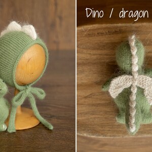 May include: A sage green knitted bonnet with a row of cream-colored spikes along the top and matching ties, accompanied by a small, matching sage green knitted dinosaur or dragon toy featuring cream-colored wings and a spiked back.