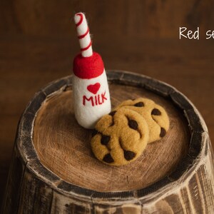 Puede incluir: Una botella de leche de fieltro con tapa roja y un coraz&oacute;n, y la palabra "MILK". Dos galletas con chispas de chocolate de fieltro est&aacute;n al lado de la botella. Los art&iacute;culos est&aacute;n sobre una superficie de madera. El texto "Red set" est&aacute; en la esquina superior derecha.