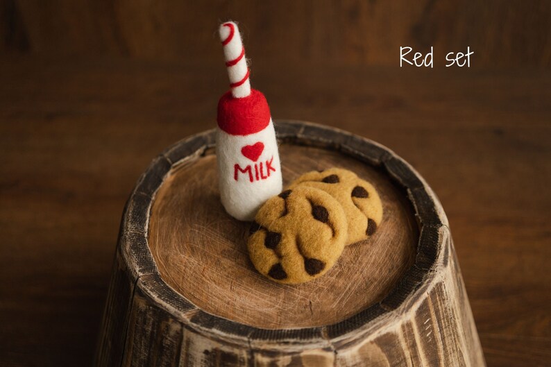 Puede incluir: Una botella de leche de fieltro con tapa roja y un coraz&oacute;n, y la palabra "MILK". Dos galletas con chispas de chocolate de fieltro est&aacute;n al lado de la botella. Los art&iacute;culos est&aacute;n sobre una superficie de madera. El texto "Red set" est&aacute; en la esquina superior derecha.