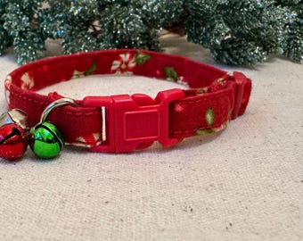 Könnte beinhalten: Ein rotes Katzenhalsband mit festlichem Blumenmuster und roter Kunststoffschnalle. Das Halsband ist mit silbernen und grünen Glöckchen verziert, perfekt für die Weihnachtszeit. Das Halsband ist etwa 2.5 cm breit.