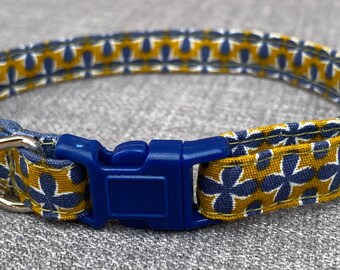 以下が含まれることがあります： 青と黄色の花柄の猫用首輪。青いプラスチック製のバックルと銀色のベルが付いています。