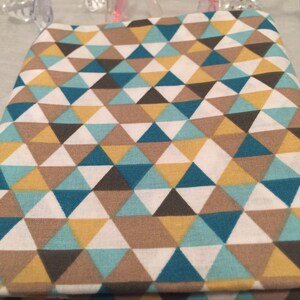 May include: Folded fabric with a geometric pattern of triangles in teal, yellow, brown, gray, and white. The fabric is likely cotton or a similar material, suitable for quilting or crafting projects. The design is modern and eye-catching.