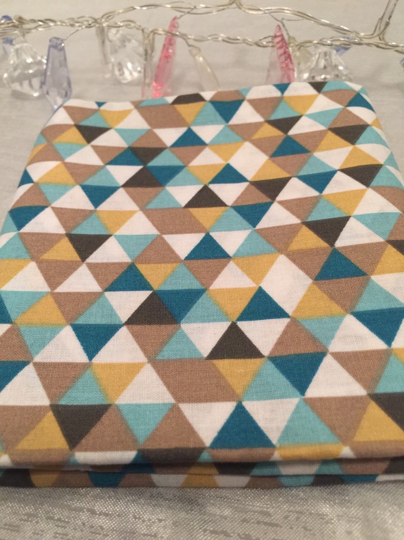 May include: Folded fabric with a geometric pattern of triangles in teal, yellow, brown, gray, and white. The fabric is likely cotton or a similar material, suitable for quilting or crafting projects. The design is modern and eye-catching.