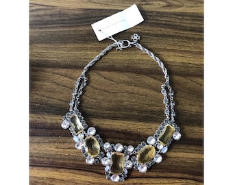May include: Silver-toned necklace with large, rectangular amber-colored stones and smaller clear crystals. The necklace has a twisted rope chain and a tag that reads "ANN TAYLOR". The jewelry is displayed on a wooden surface.
