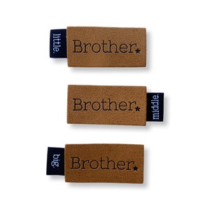 May include: Three brown leather labels with the word "Brother" and a star printed on them. Each label has a black fabric tag attached with the words "little", "middle", and "big" printed on them.