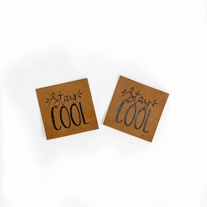 Peut inclure: Deux patchs en cuir marron avec le texte "Stay Cool" en lettres noires.