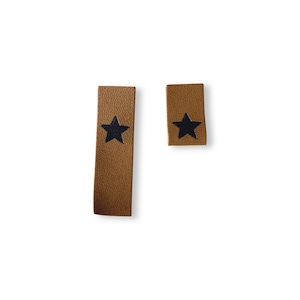 May include: Two brown leather tags with black star designs. One tag is rectangular and longer than the other. The tags are set against a white background.