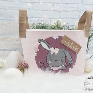 Op de afbeelding: Roze paasmand met bruine handvatten en een konijnenontwerp. De mand heeft een gepersonaliseerd naambordje met de tekst "Victoria".