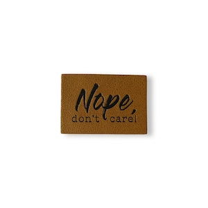Puede incluir: Un parche de cuero marrón con el texto "Nope, don't care" en letras negras.