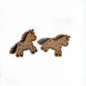 May include: Two brown leather unicorn patches with black outlines and white details. The unicorns are facing different directions and have a whimsical design.