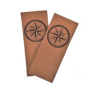 Könnte beinhalten: Zwei braune Leder-Lesezeichen mit einem aufgedruckten Kompass-Design.