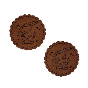 May include: Two brown leather round coasters with a black outline of a donkey with hearts around it.