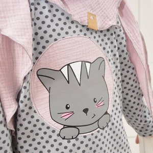 Pode incluir: Uma camisa de manga comprida cinza e branca com bolinhas e um desenho de gato rosa. A camisa tem uma gola rosa e um cachecol rosa a condizer. O texto "LUI & LEV" est&aacute; impresso na camisa.