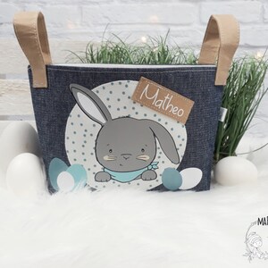 Op de afbeelding: Een blauwe denim paasmand met een konijnenontwerp en de naam "Matheo" op een bruin label. De mand heeft twee bruine handvatten.