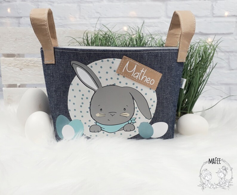 Op de afbeelding: Een blauwe denim paasmand met een konijnenontwerp en de naam "Matheo" op een bruin label. De mand heeft twee bruine handvatten.