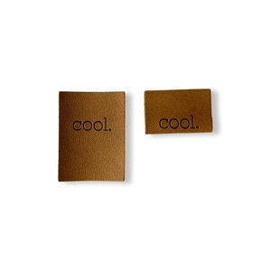 Peut inclure: Deux étiquettes en cuir marron avec le mot "cool." en relief en noir.