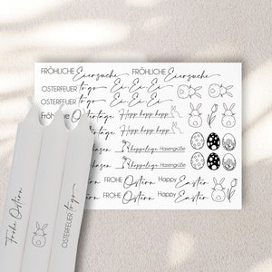 Könnte beinhalten: Ein Blatt weißes Papier mit schwarzen Stempeln mit Ostern-Motiven. Die Stempel zeigen Hasen, Eier, Blumen und Text in Deutsch und Englisch, wie "Frohe Ostern" und "Happy Easter".