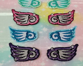 May include: A collection of eight embroidered wing patches in various colors. The patches include pairs of teal, pink, blue, and purple wings with silver and black detailing. The patches are arranged on a pastel background with a star pattern.