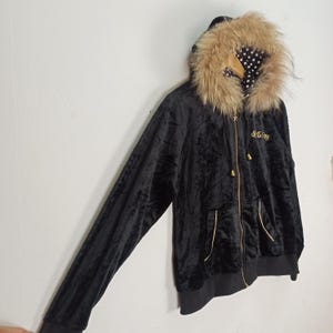 May include: Black velvet hooded jacket with a faux fur trim around the hood. The jacket features a gold zipper, pockets, and the embroidered text "So Many". The lining of the hood is white with black polka dots.
