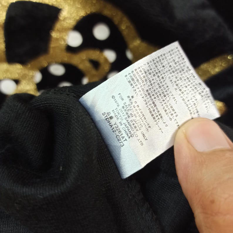 May include: Close-up of a black fabric with a white tag. The tag has Japanese text and the text "FOR SALE IN JAPAN ONLY". The fabric has a gold pattern with white polka dots.