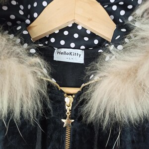 May include: Black hooded jacket with a gold zipper and a star-shaped charm. The jacket features a faux fur trim and a polka dot lining. The label reads "Hello Kitty".