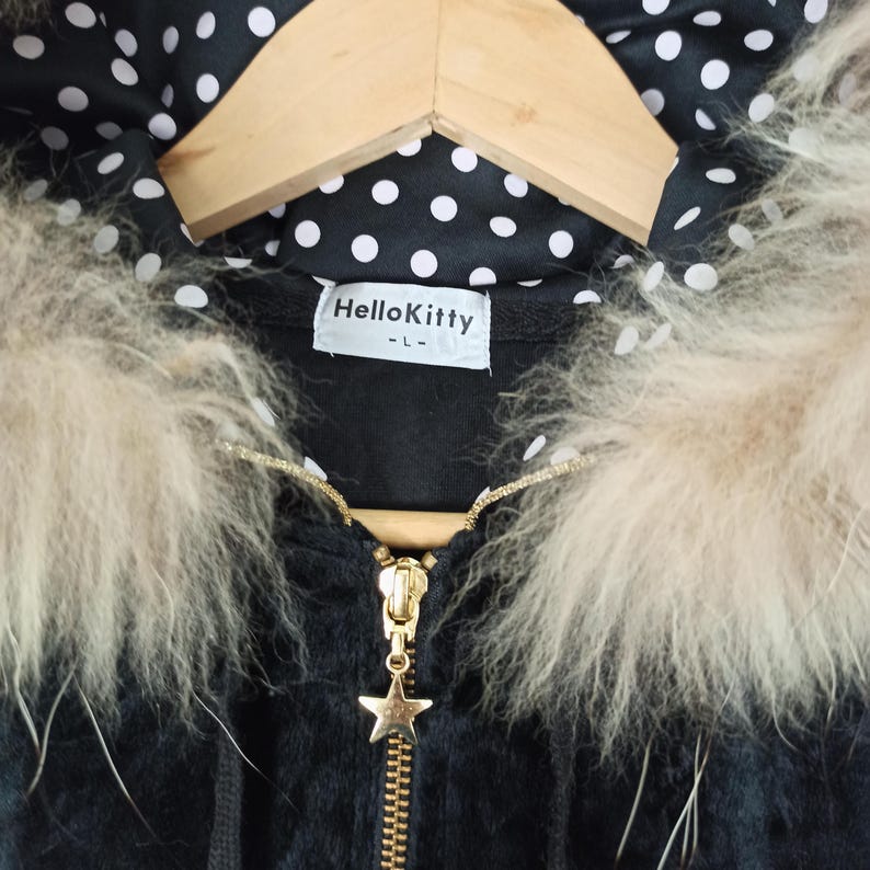 May include: Black hooded jacket with a gold zipper and a star-shaped charm. The jacket features a faux fur trim and a polka dot lining. The label reads "Hello Kitty".