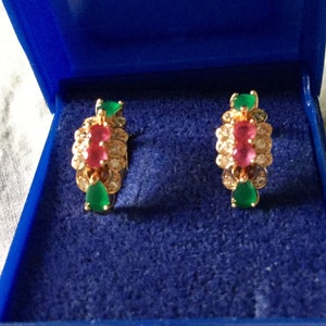 Peut inclure: Une paire de boucles d'oreilles dorées avec un motif en grappe. Chaque boucle d'oreille présente une pierre rose centrale, entourée de pierres claires et ornée de pierres vertes en forme de goutte. Les boucles d'oreilles sont présentées dans un écrin bleu.
