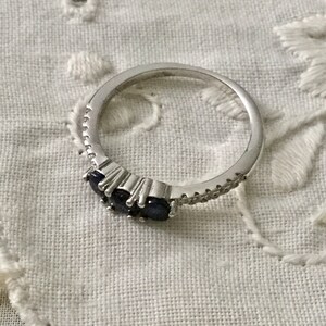May include: A silver ring featuring three dark blue gemstones and a row of small clear stones.