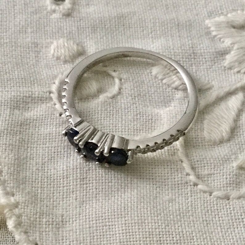 May include: A silver ring featuring three dark blue gemstones and a row of small clear stones.