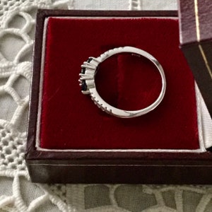May include: A silver ring with three black gemstones and small white gemstones set in a band.