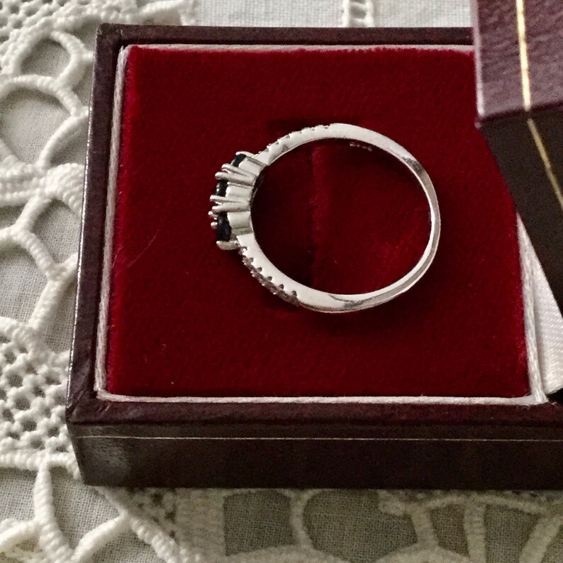 May include: A silver ring with three black gemstones and small white gemstones set in a band.