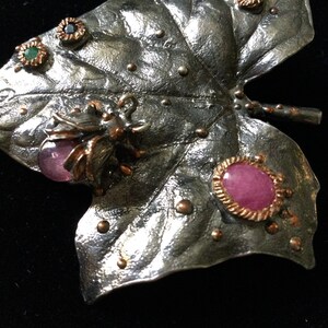 May include: A silver leaf brooch with pink and green gemstone accents and a detailed beetle design.